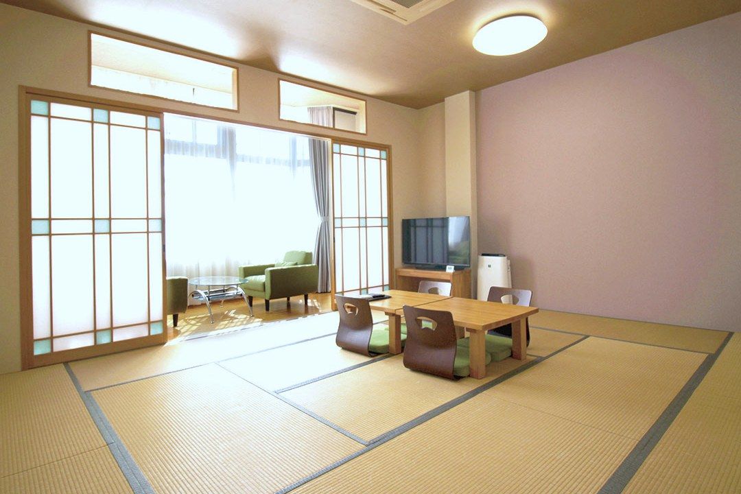 広い和室に座卓と座椅子4脚、窓辺にソファ